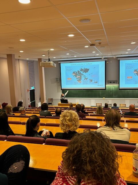 Vanessa Lampe standing in the front of a lecture hall and presenting a picture of the map of Svalbard.