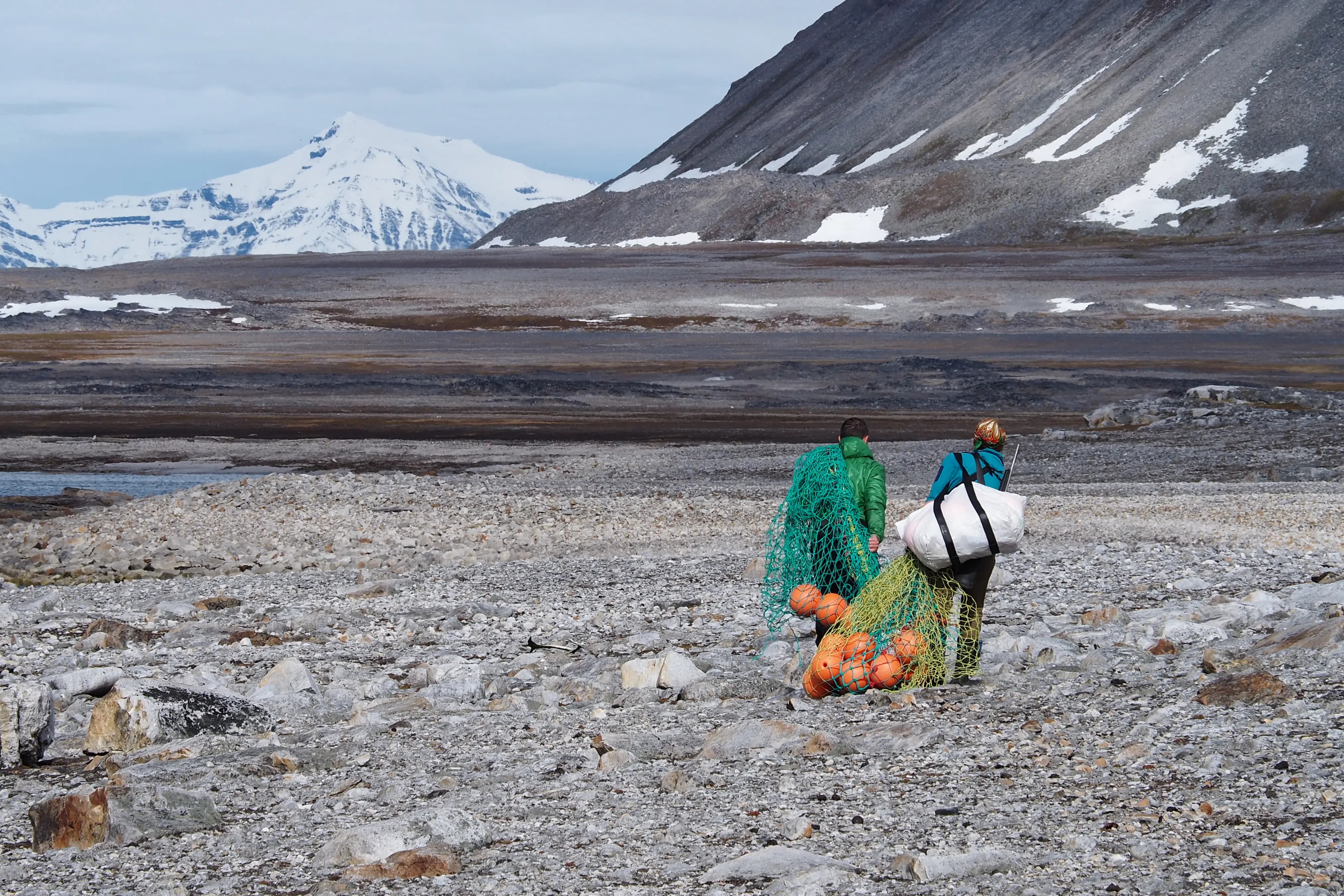 Two people carrying bags of marine litter in a rocky beach landscape.