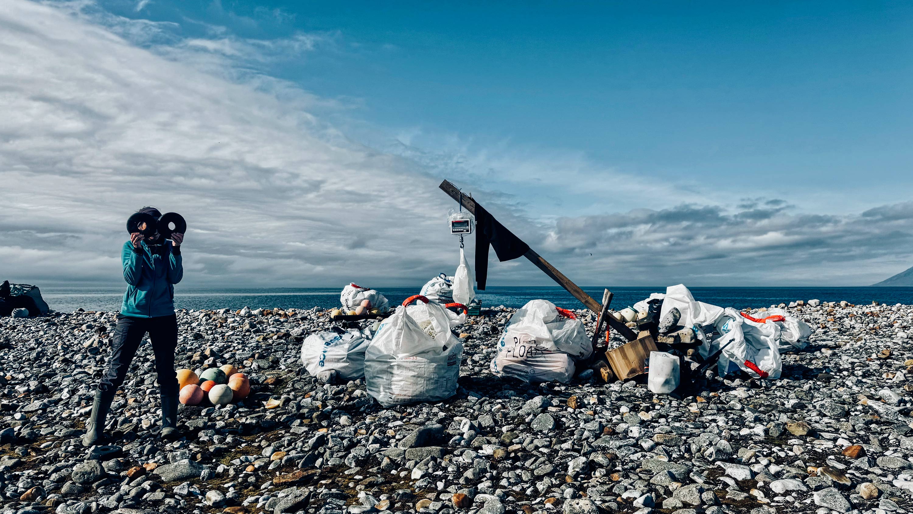 On a rocky beach a person sets up a temporary marine litter weighing station.