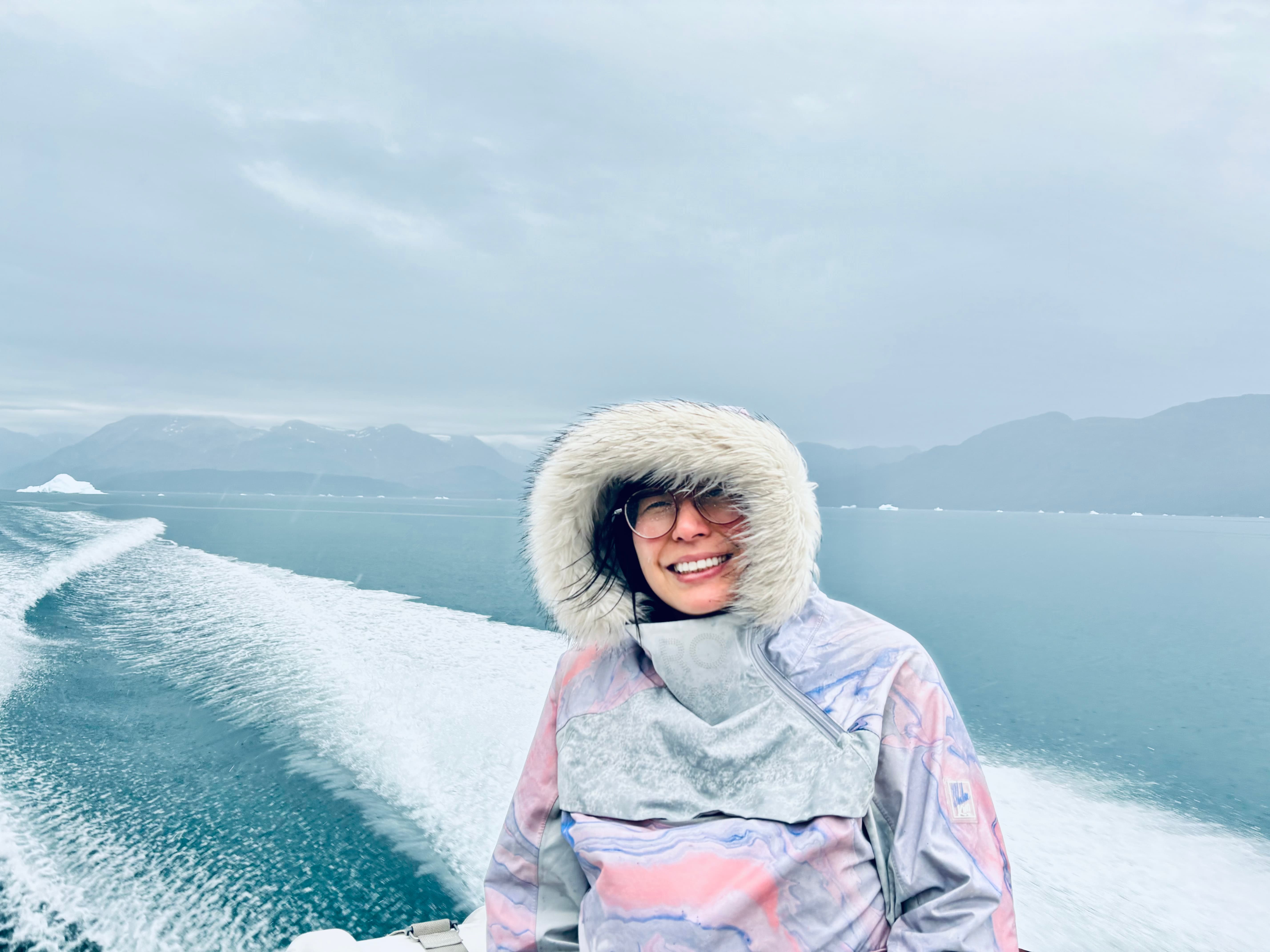 Christine Liang in a winter jacket on a boat that sails through a sea with a mountain in the background.