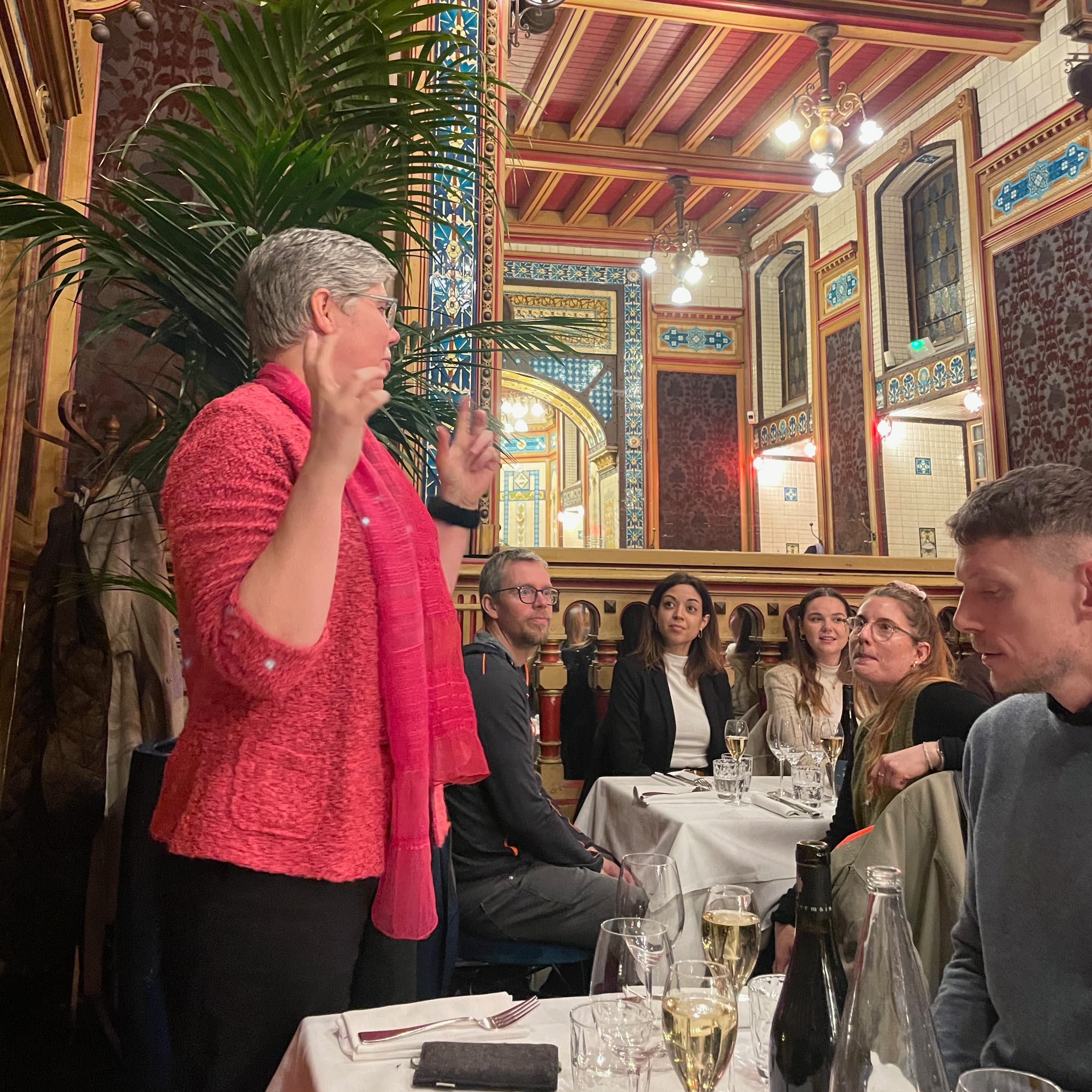 In a restaurant with mirrors and ornaments on the wall, Thora Herrmann gives a speech with ICEBERG people listening.