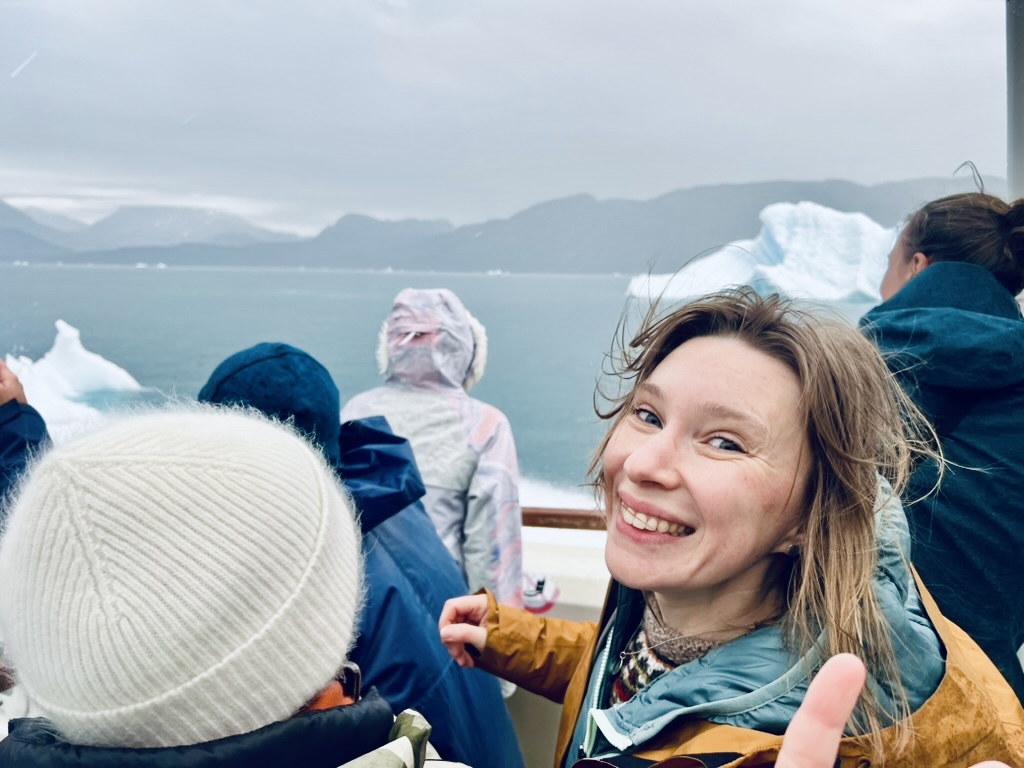 A photo of Tahnee Prior smiling for the camera in a boat that sails in an Arctic environment in the middle of small icebergs.