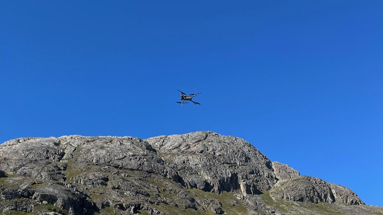 A drone flying on a rocky hill with blue sky above.