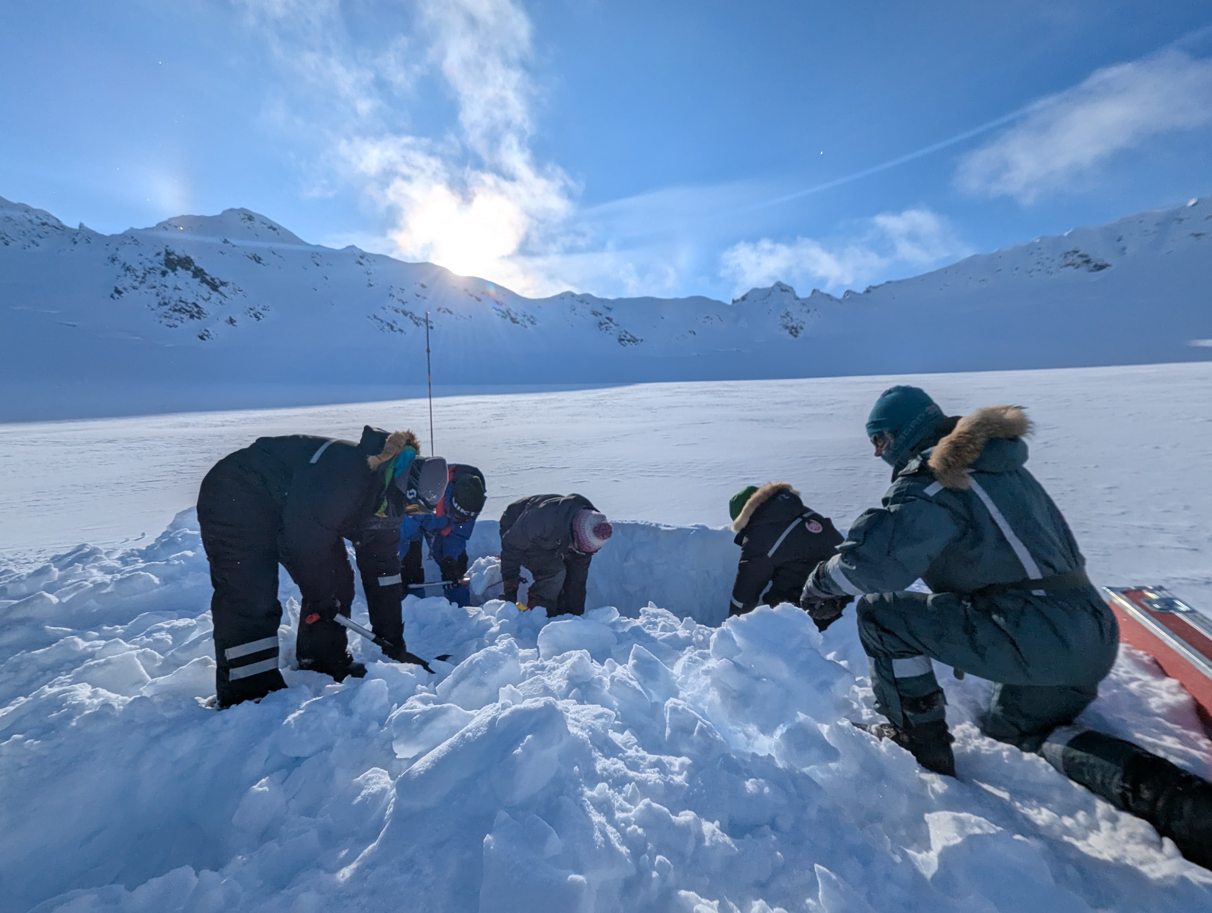 Five researchers in full winter gear digging a hole in the snow.