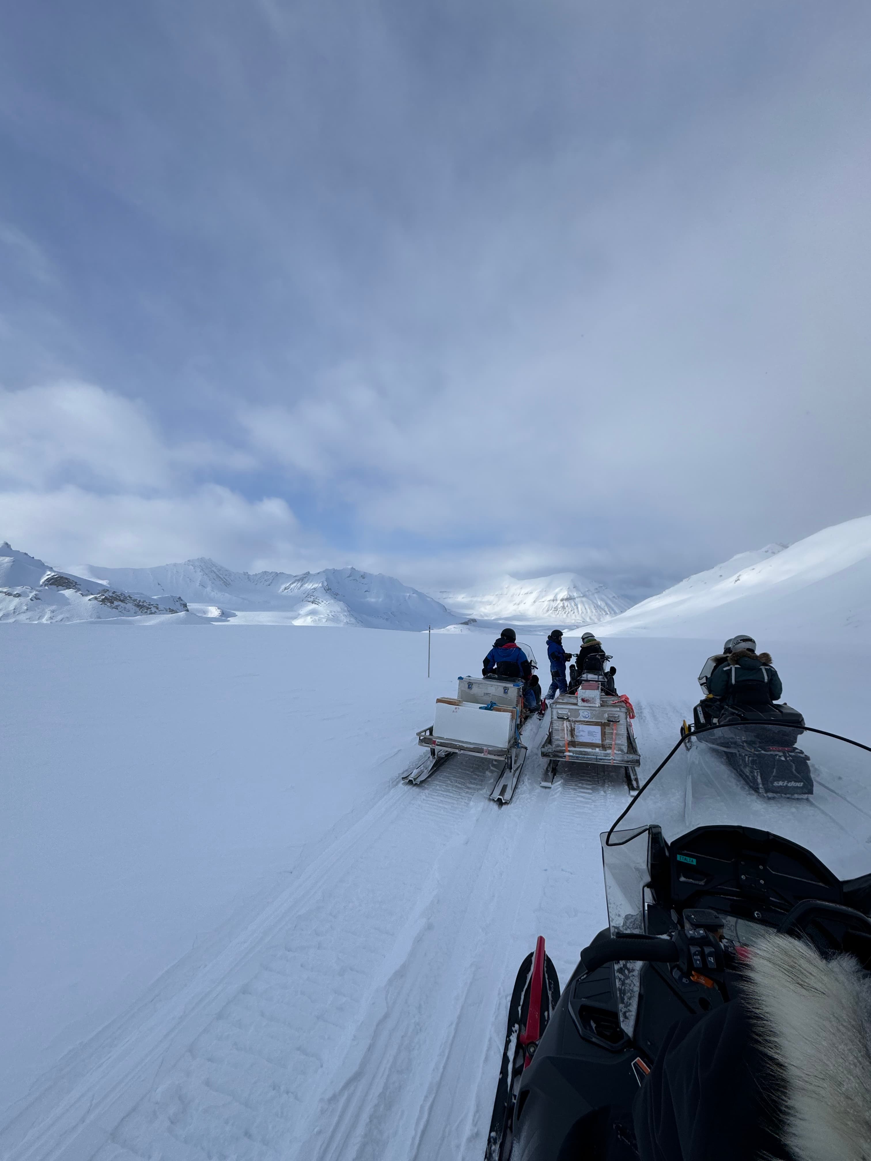 Researchers riding snow mobiles on a snowy landscape in Ny-Ålesund.