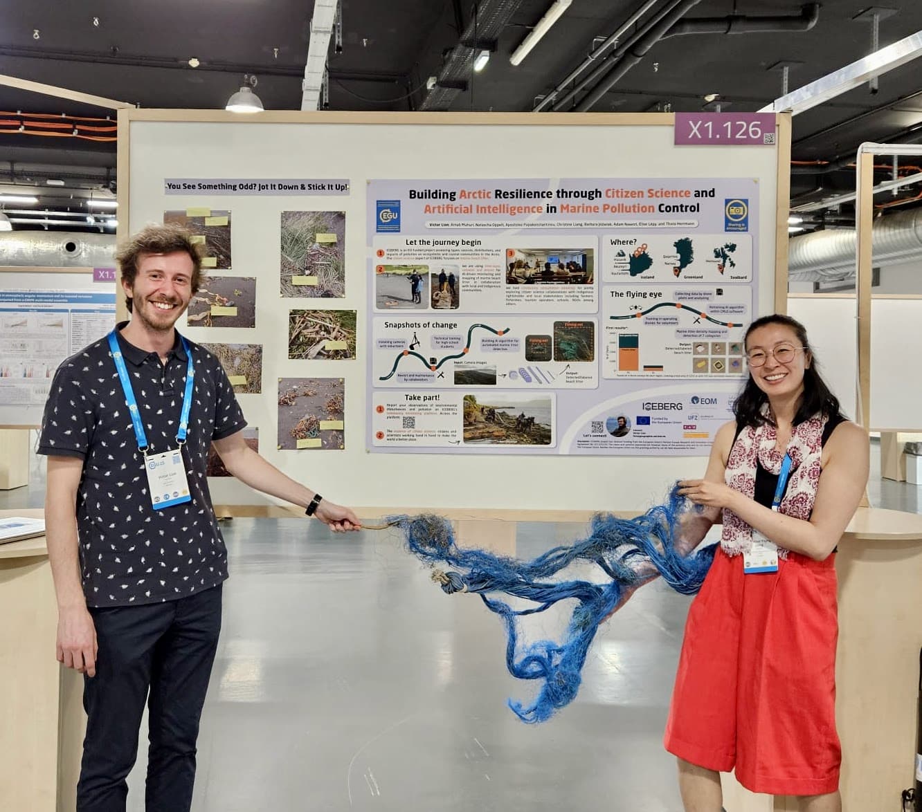 Victor Lion and Christine Liang posing in front of Victor's scientific poster in the conference. They're holding blue, rope-like material between them and smile for the camera.