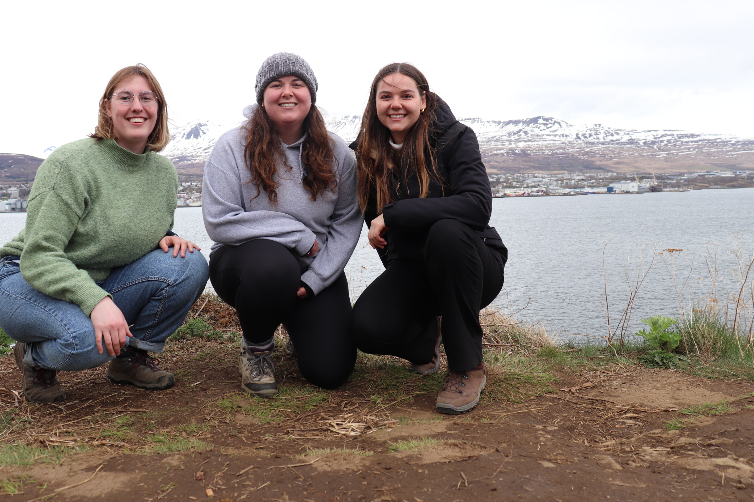 Anna Lauenburger, Isobel Stuart and Melanie Mobley stand on the ground in front of a fjord.