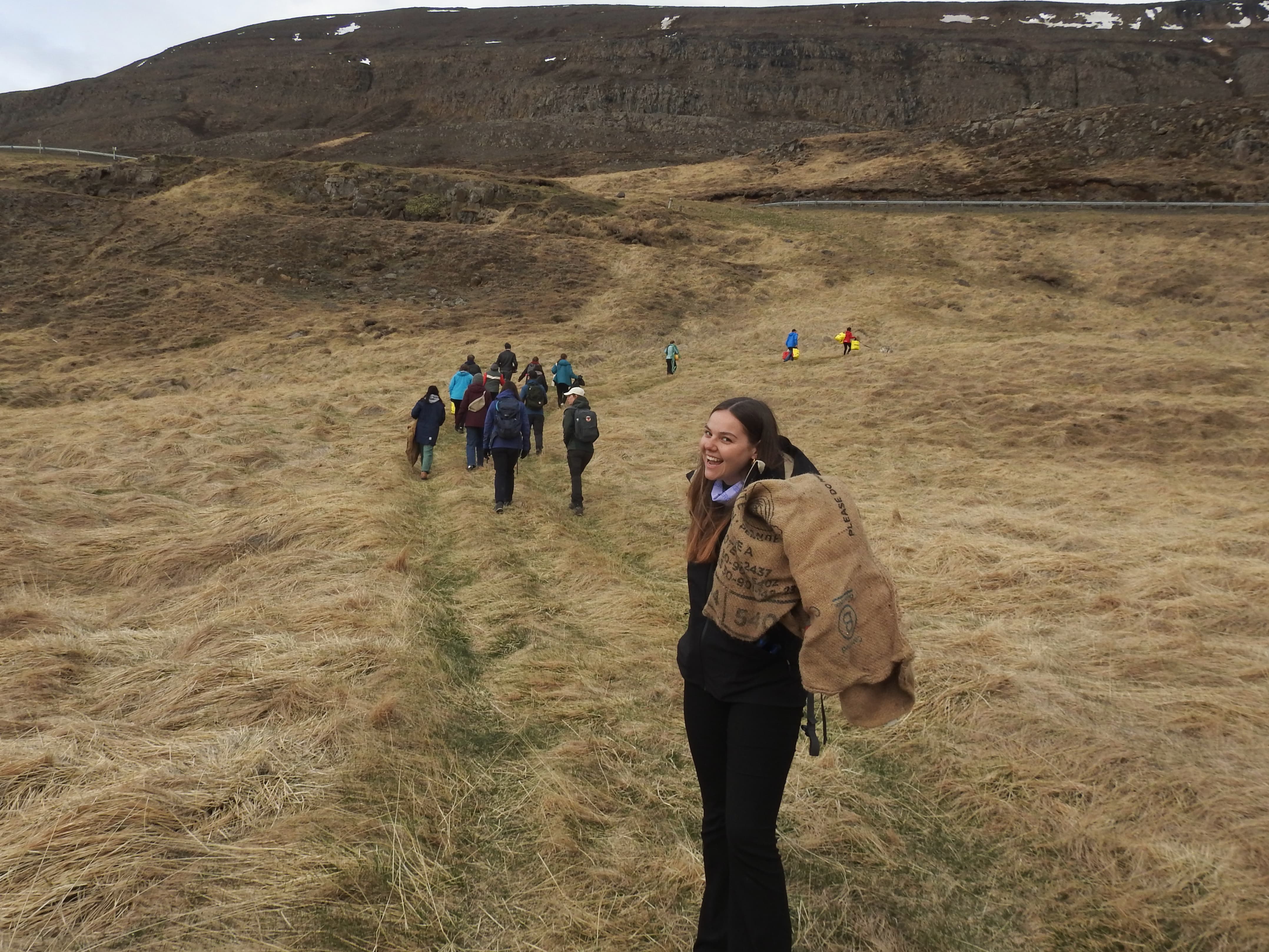 On a plain landscape, Melanie Mobley smiles for the camera. Other volunteers walking ahead towards a plain hill.
