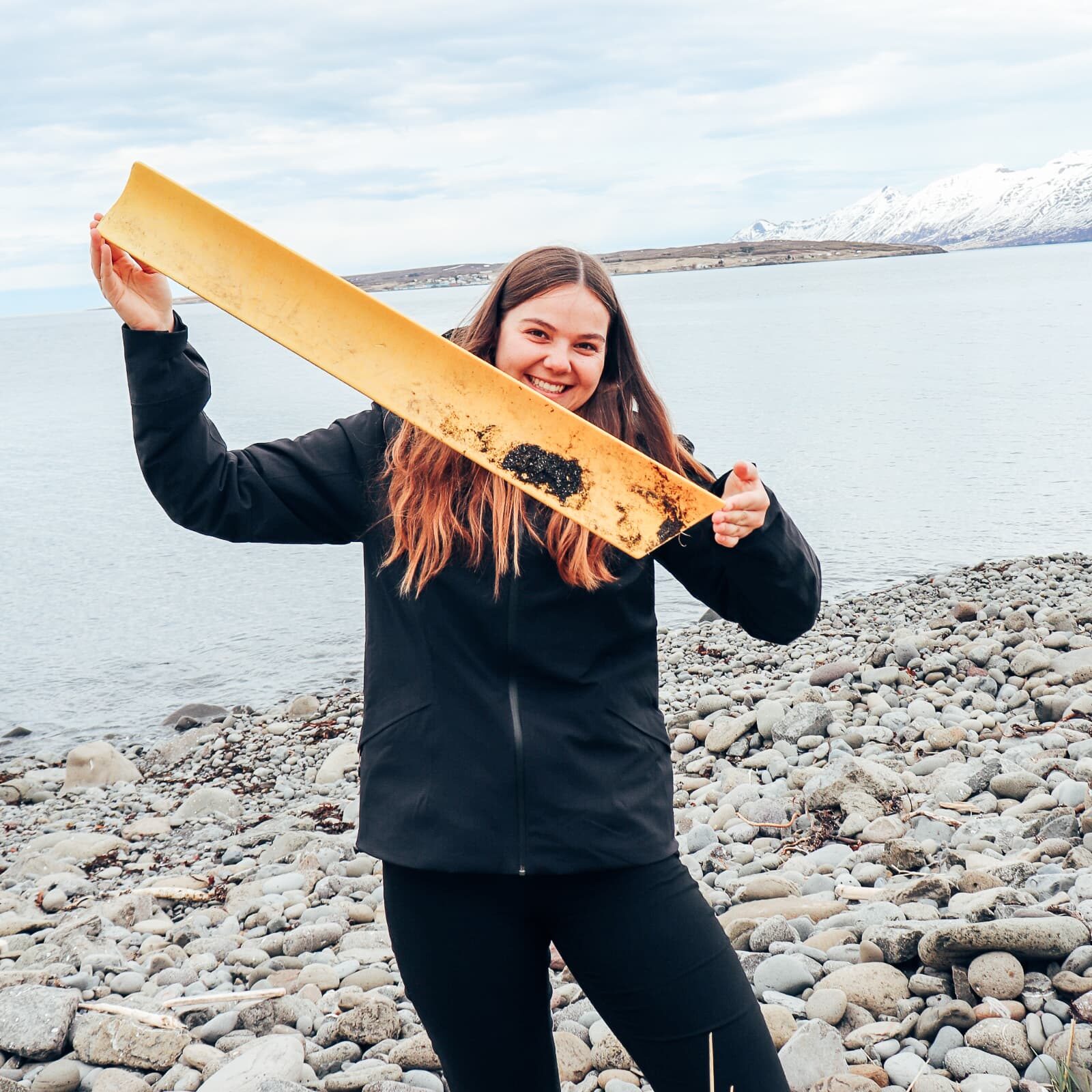 Melanie on the rocky beach in Akureyri, holding a large yellow piece of plastic litter.