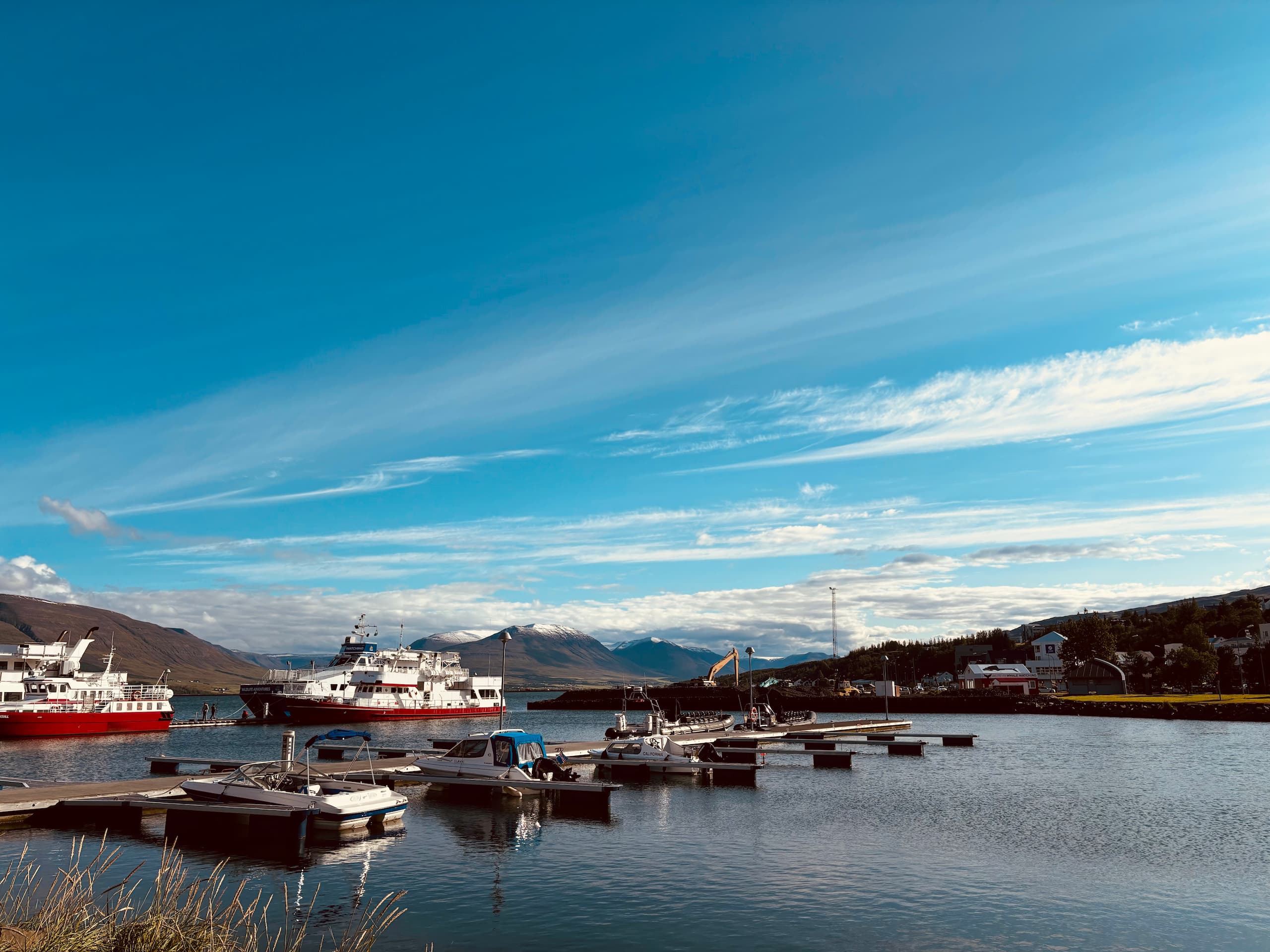 A ship harbour in Akureyri, Iceland, with two ships and multiple smaller boats. Snowy mountains in the background.