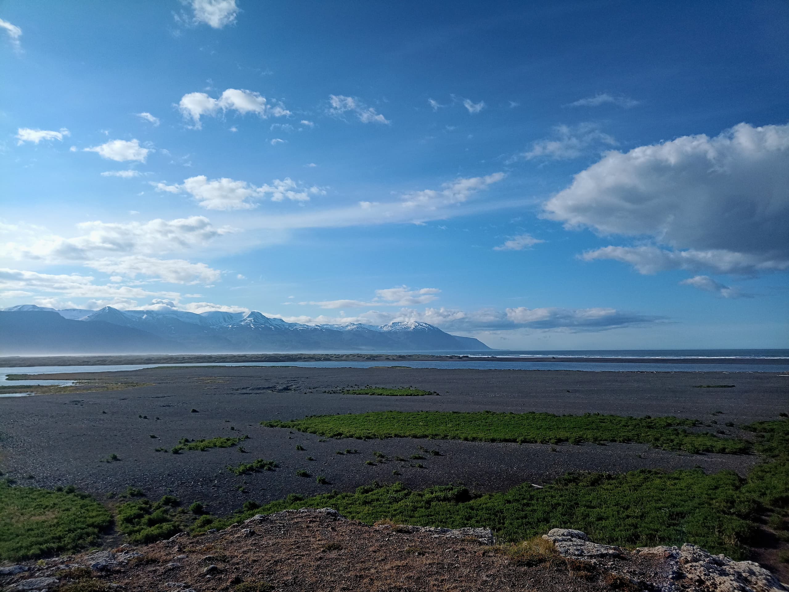 A rocky beach in Húsavík with snowy mountains in the background.