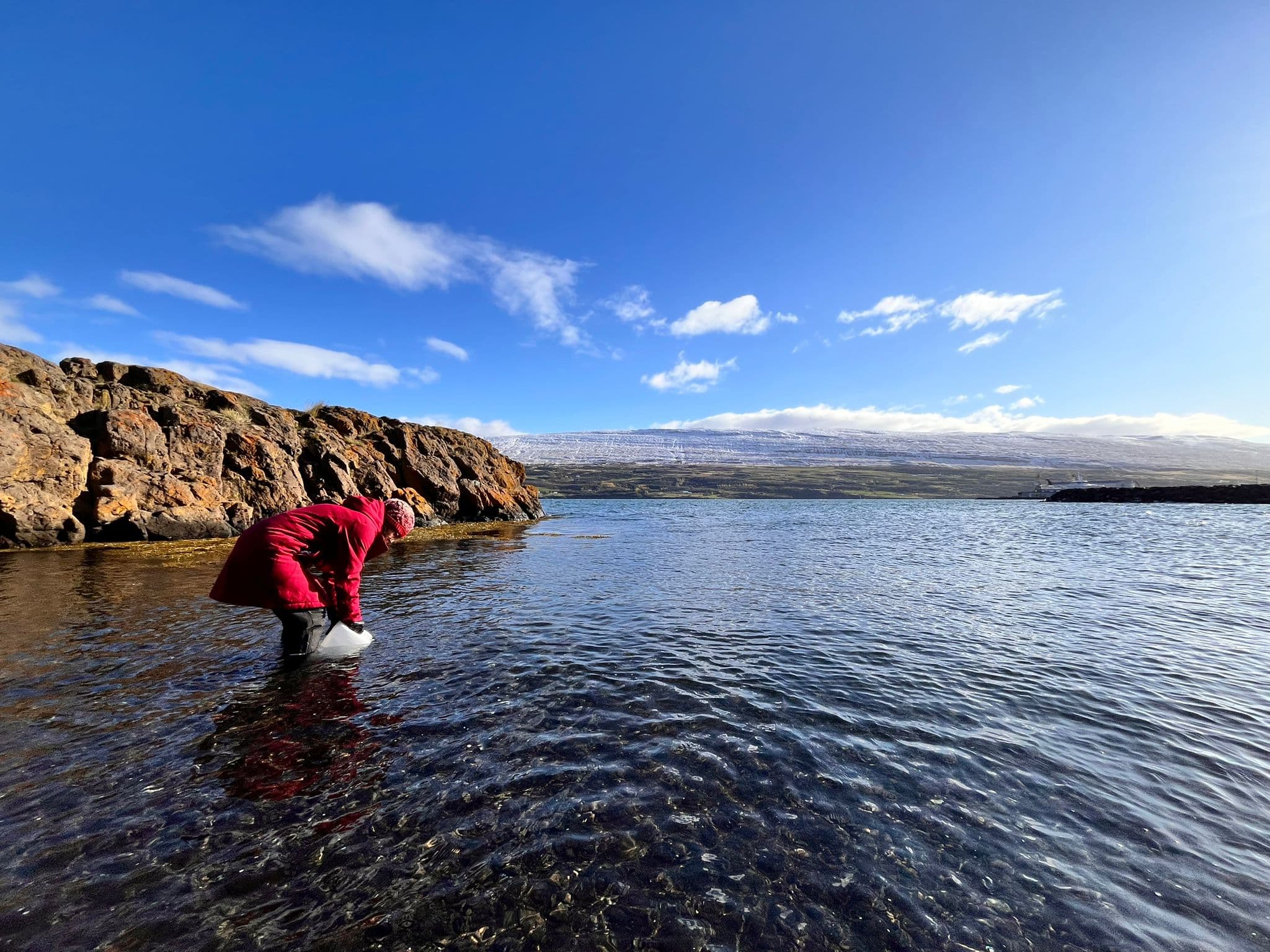 Christa Marandino standing in the water in a fjord, collecting water in a big bottle.