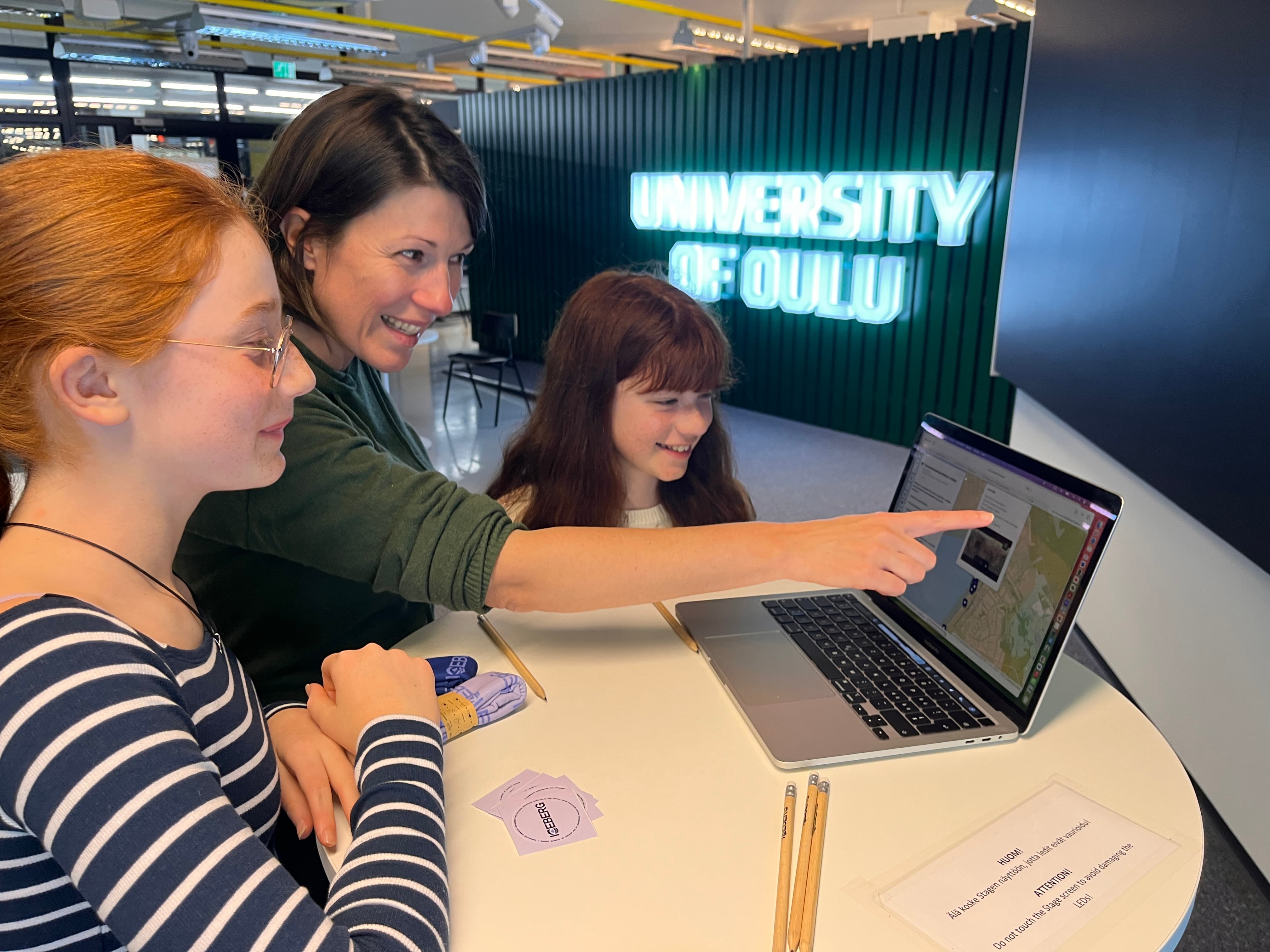 Élise Lépy shows two children something on a laptop screen. All three smile.