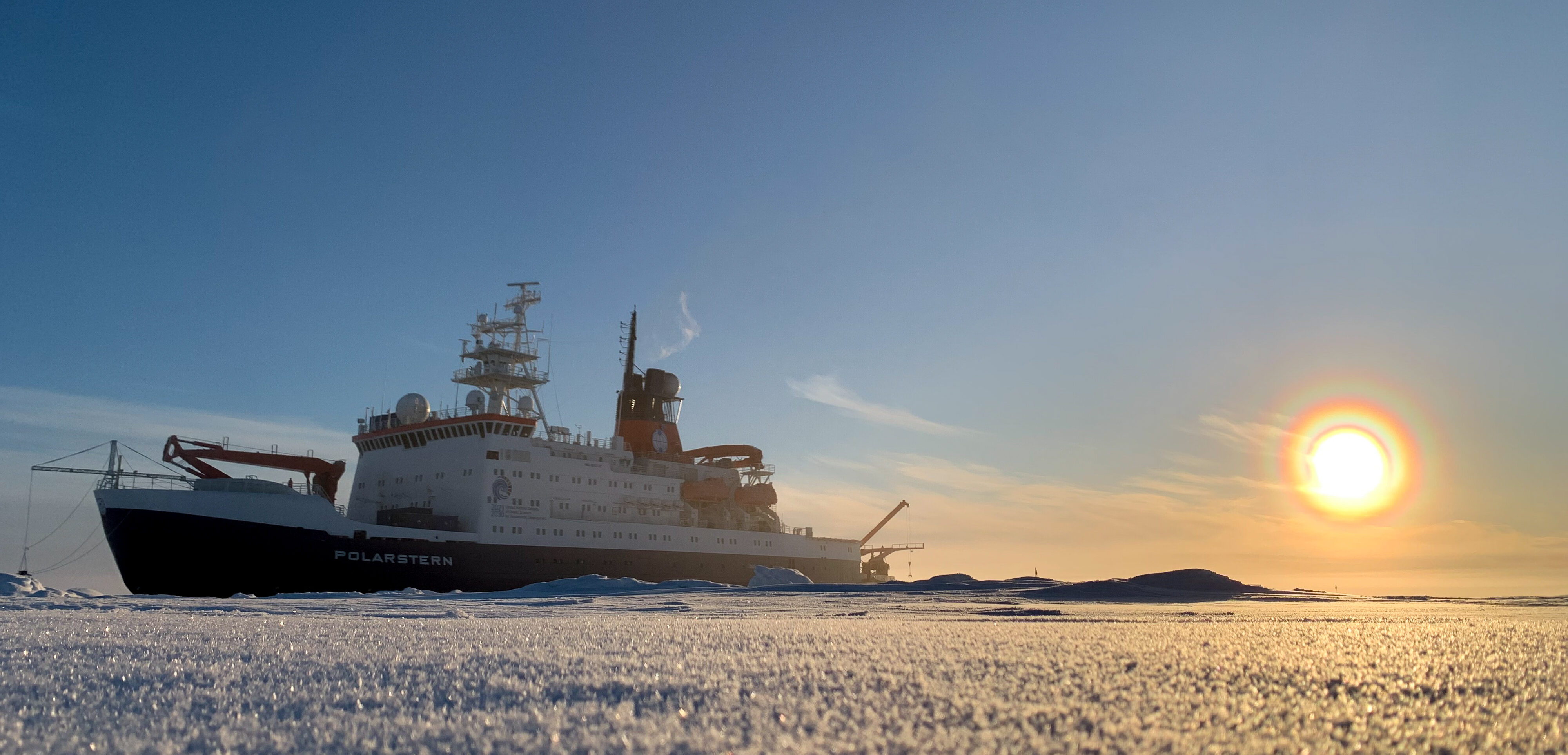 Icebreaker Polarstern on Arctic sea ice with low sun near the horizon.