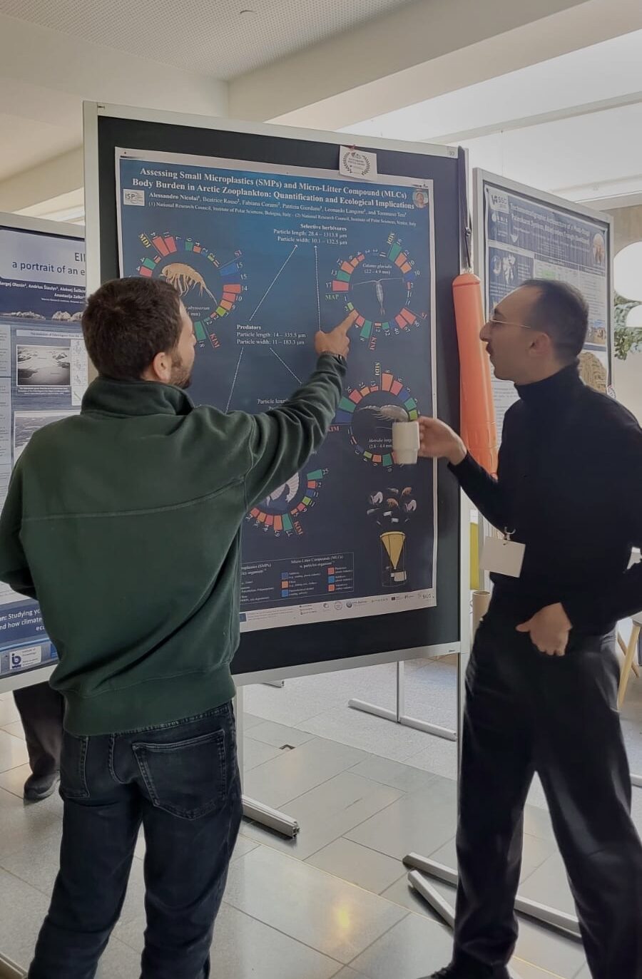 Alessandro Nicolai explains a scientific poster on microplastics in Arctic zooplankton to Dr. Francesco Paladini de Mendoza during a conference session.
