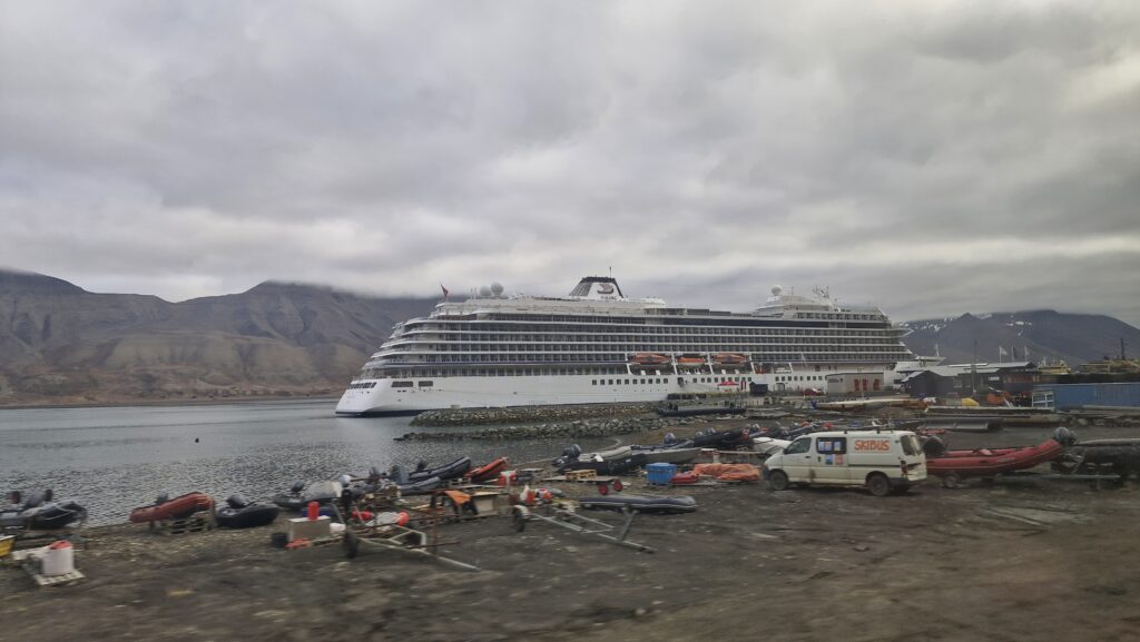 A large cruise ship in a marina, large mountains behind it.